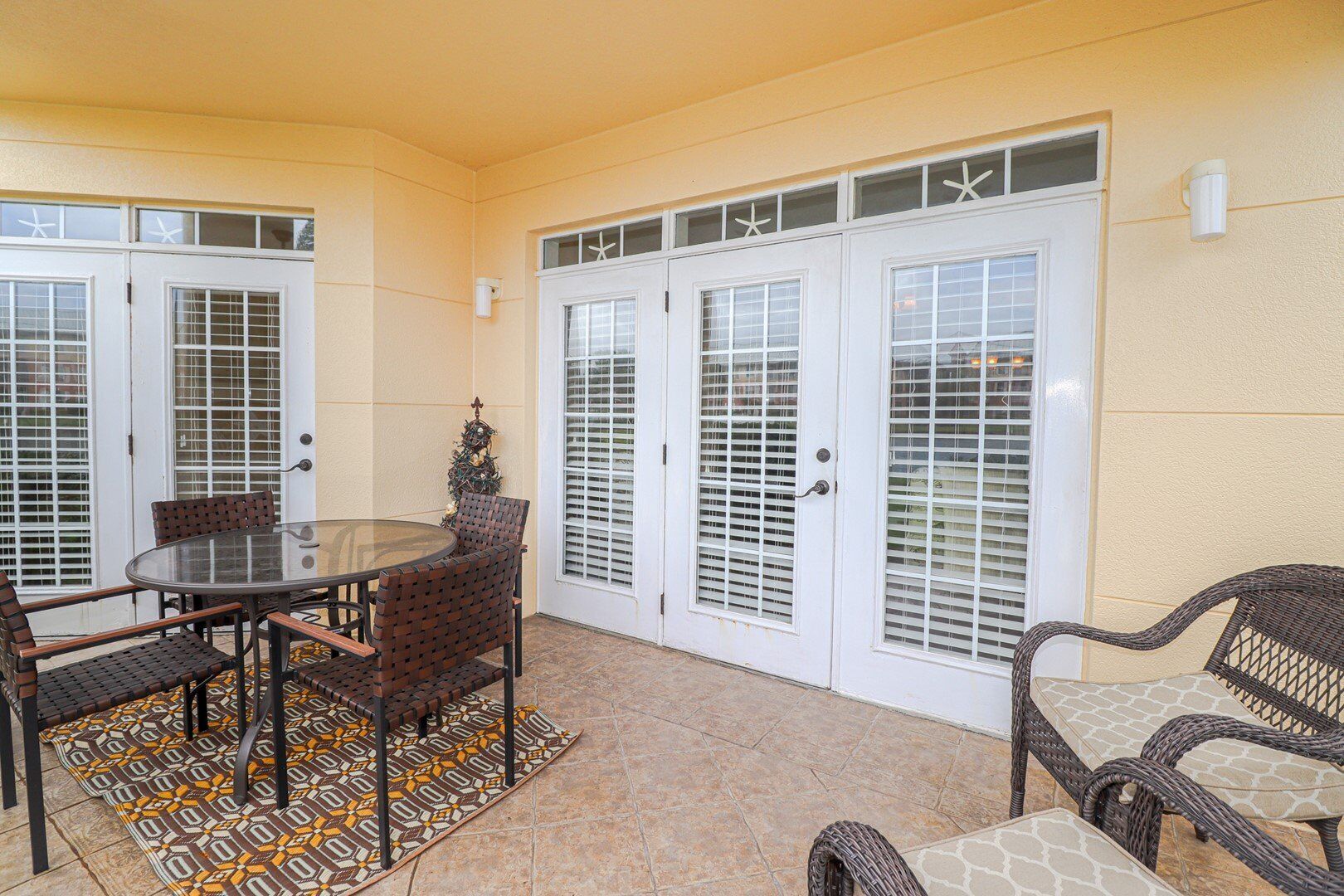 A covered patio with a glass table and wicker chairs, white doors with glass panels, and a decorative Christmas tree.