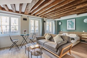 A cozy room with a wooden ceiling, a sofa, a bed, and a dining table with chairs. - Charming Studio Center of Paris-montorgueil (Paris)