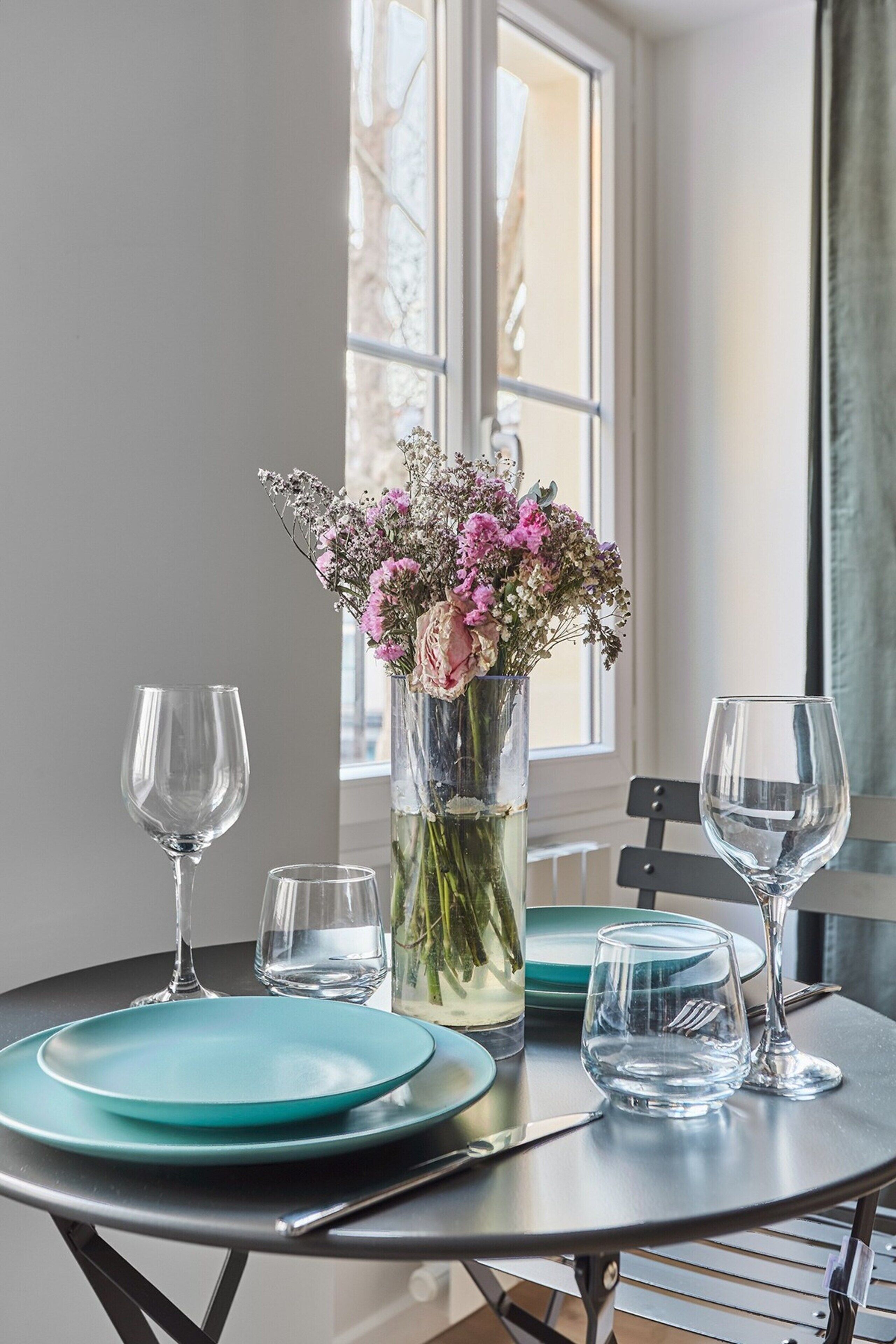 Un tavolo da pranzo con un vaso di fiori, due piatti e due bicchieri da vino.