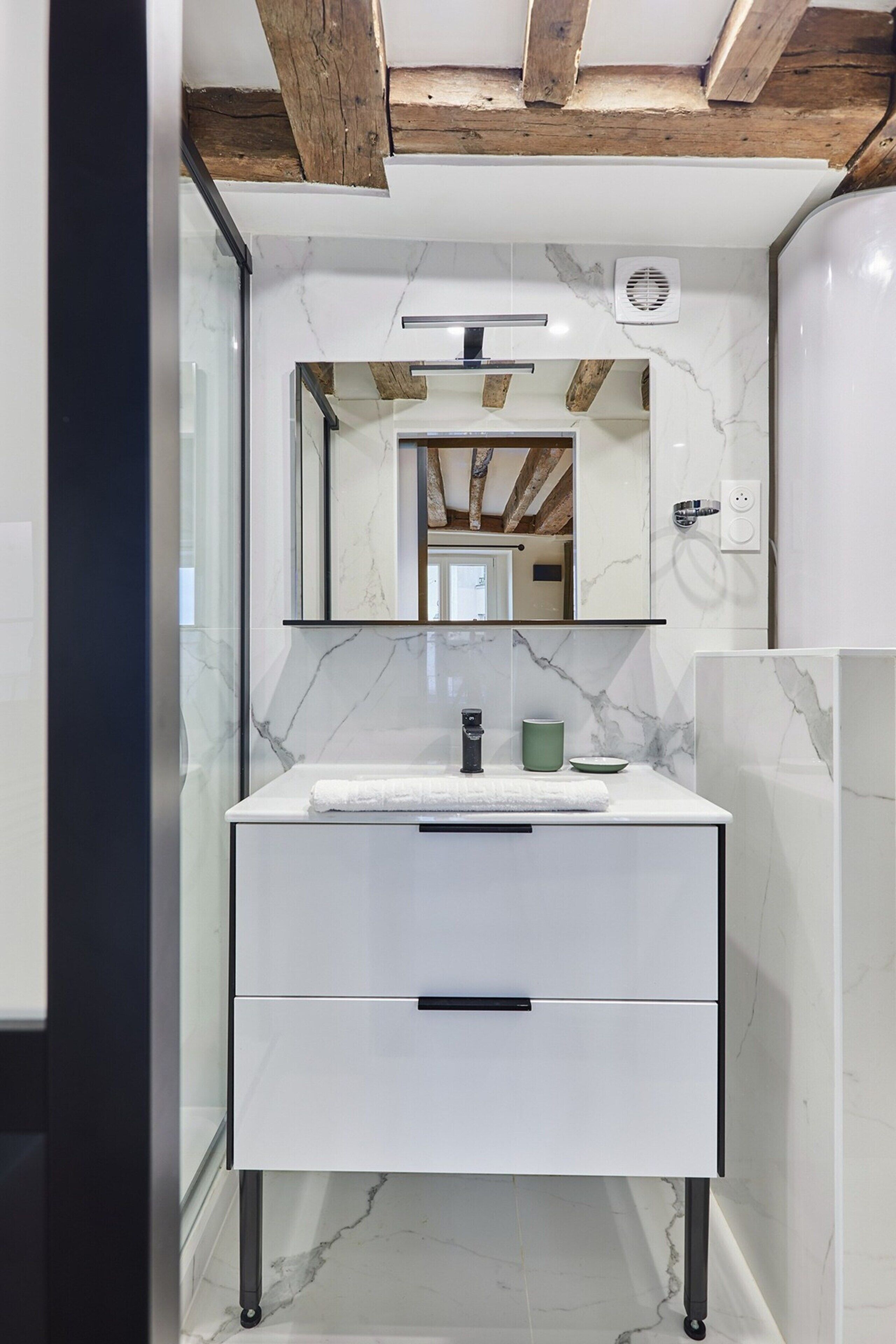 A modern bathroom with a white marble sink, a mirror above it, and wooden beams on the ceiling.