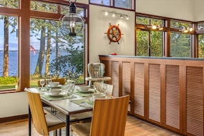 A dining area with a view of the water, wooden furniture, and a ship's wheel decoration. - Puzzle Point Lodge in Poulsbo (Poulsbo)