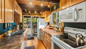 A modern kitchen with wooden cabinets, a stainless steel sink, a white refrigerator, a microwave, and a stove. - Fir Tree Cabin in Packwood (Packwood)