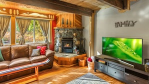 A cozy living room with a stone fireplace, a leather sofa, and a television. - Fir Tree Cabin in Packwood (Packwood)