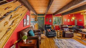 A cozy living room with a brown leather sofa, a black leather armchair, and a wooden coffee table. A red wall and wooden ceiling beams are visible. - Fir Tree Cabin in Packwood (Packwood)
