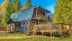 A two-story cabin with a metal roof, wooden deck, and a staircase leading to the upper level. - Fir Tree Cabin in Packwood (Packwood)