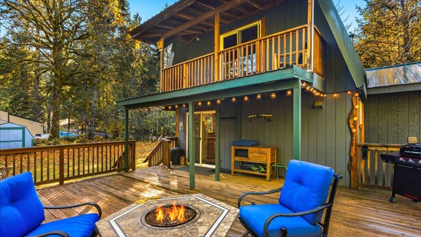 A wooden deck with a fire pit, two blue chairs, and a covered seating area with a table and bench. - Fir Tree Cabin in Packwood (Packwood)