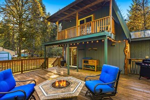 A wooden deck with a fire pit, two blue chairs, and a covered seating area with a table and bench. - Fir Tree Cabin in Packwood (Packwood)
