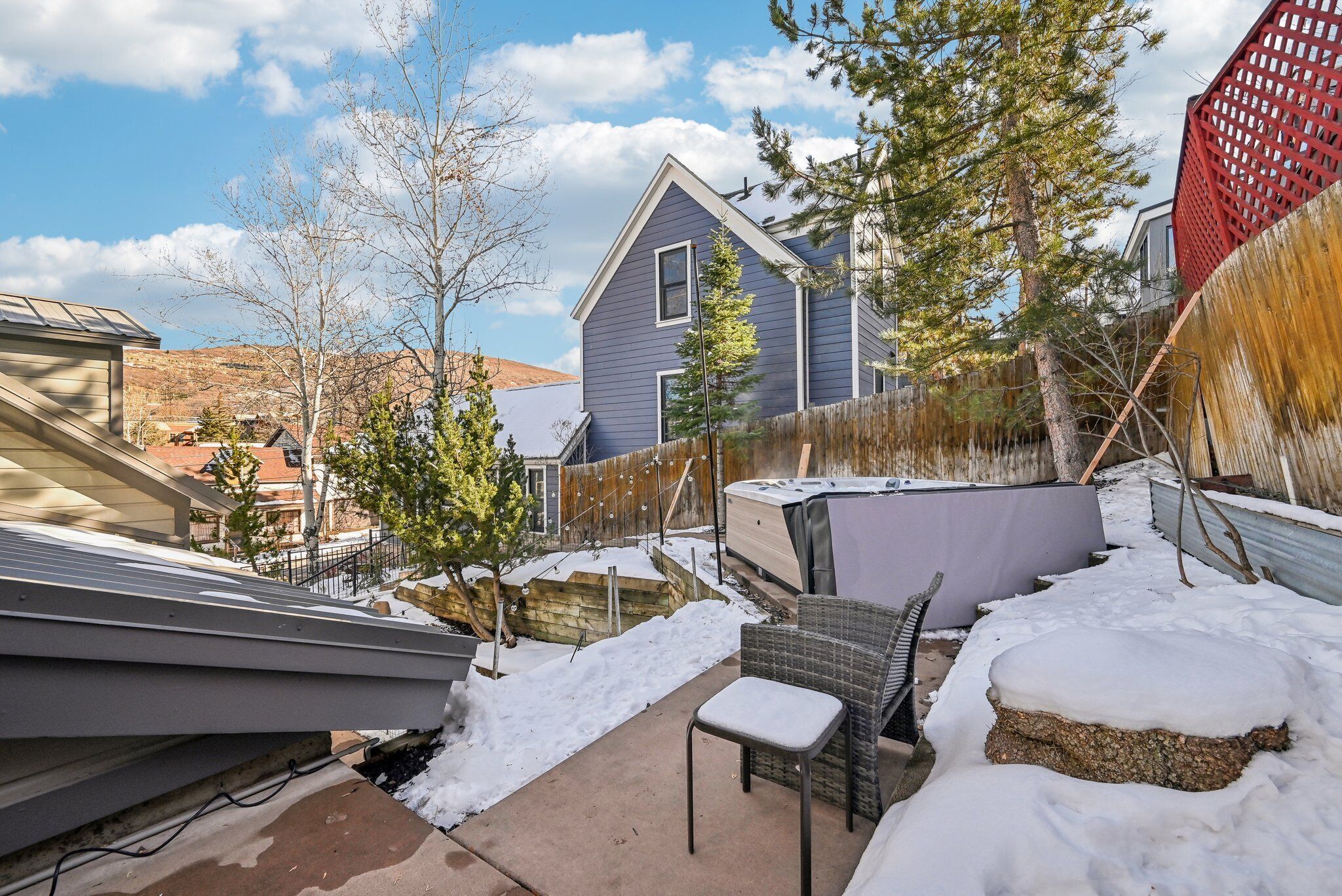Un jardin à l’arrière d’une maison, avec une terrasse couverte, un jacuzzi et une clôture en bois.
