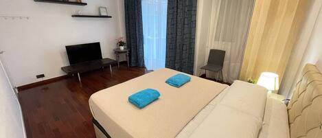 Et hotelværelse med seng, fjernsyn, skrivebord og stol.