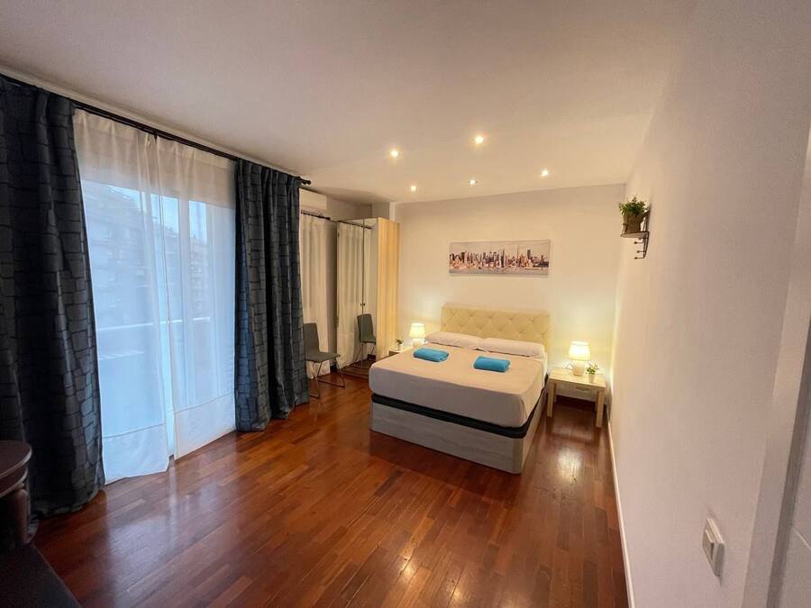 Habitación de hotel con una cama grande, vistas a la ciudad, una mesita de noche con lámpara y una silla.