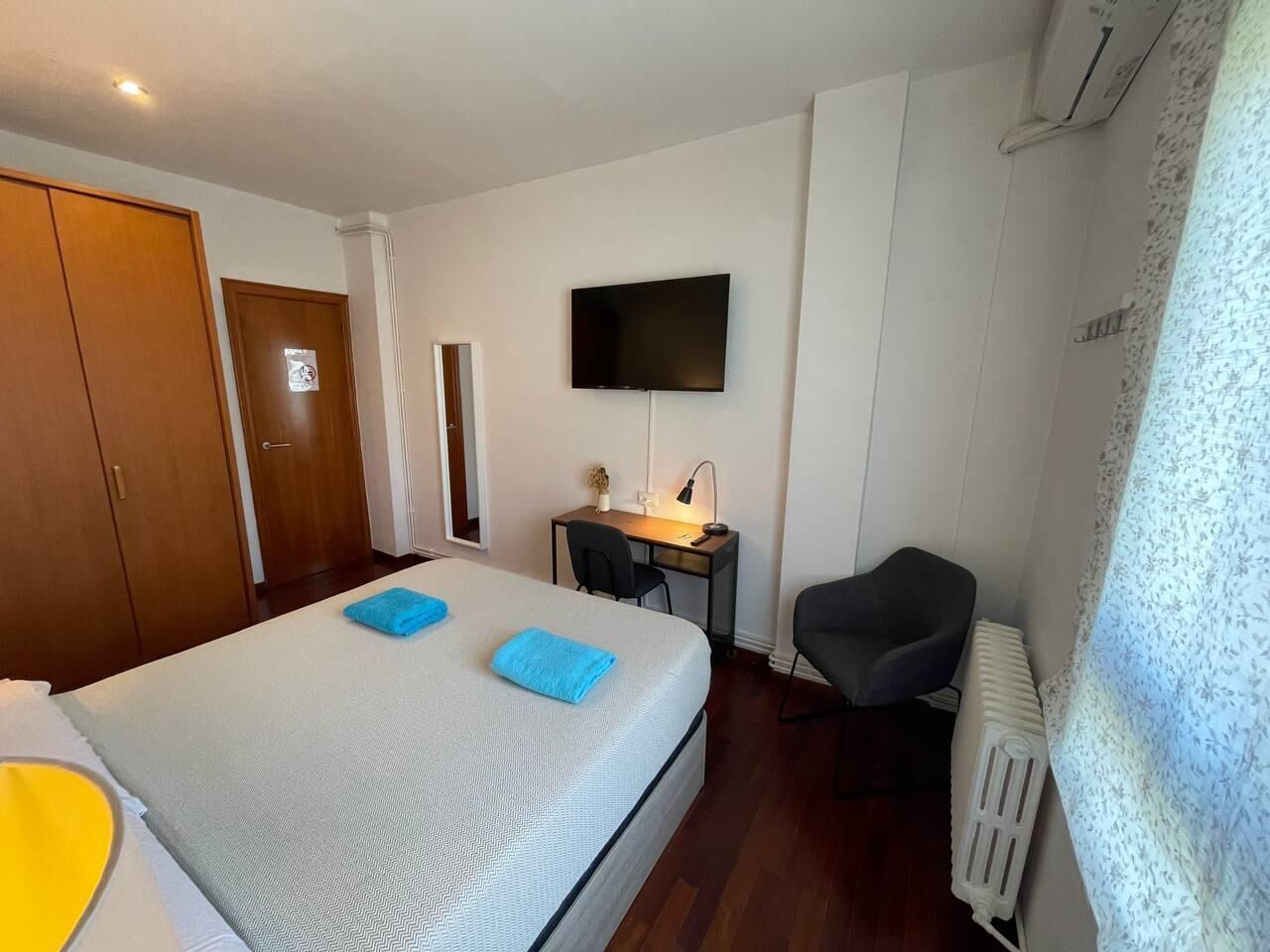 Una habitación de hotel con cama, escritorio, silla, televisor y armario.