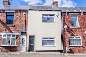 A two-story residential building with a flat facade, a front door, and a small front garden. - Toast Stays - The Garthhill (Ferryhill)