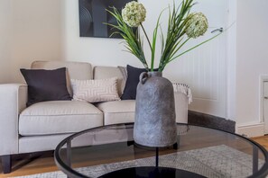 A living room with a sofa, a vase with flowers, and a glass coffee table.