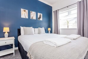 A hotel room with a large bed, two bedside tables, a window with curtains, and three wall-mounted artworks. - Toast Stays - The Garthhill (Ferryhill)