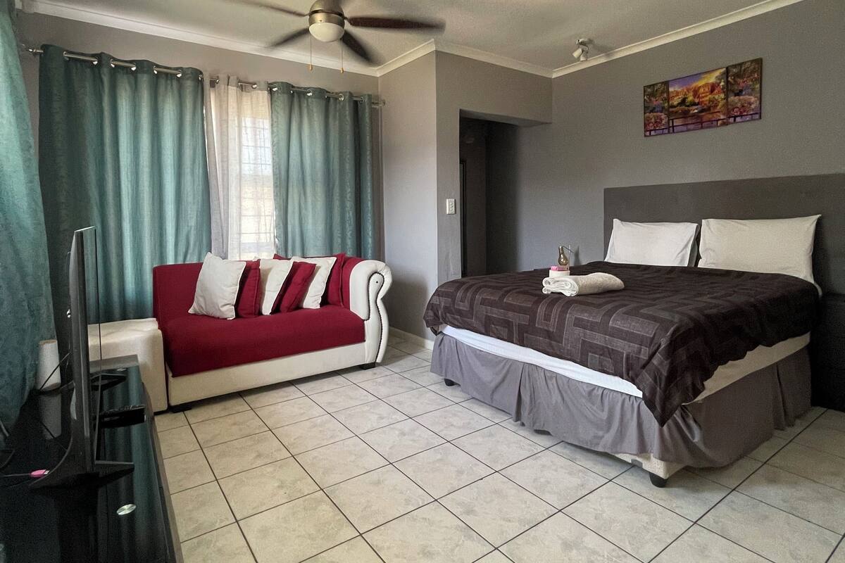 A hotel room with a bed, a sofa, a ceiling fan, and a painting on the wall.