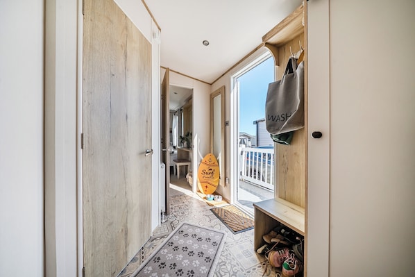 A hallway with a wooden door, a view of a balcony with a surfboard, and a shoe rack. - Seaview,sleeps 4to6,pet Friendly, Parking (Wareham)