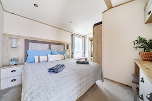A bedroom with a bed, bedside tables, a nightstand, a potted plant, and a window with curtains. - Seaview,sleeps 4to6,pet Friendly, Parking (Wareham)