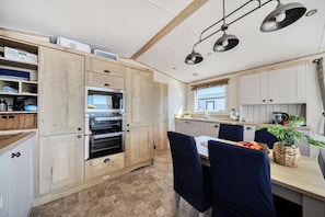 A modern kitchen with wooden cabinetry, a built-in oven, and a dining area with a table set for two. - Seaview,sleeps 4to6,pet Friendly, Parking (Wareham)