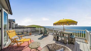 A wooden deck with outdoor furniture, including chairs and a table, overlooking a body of water.