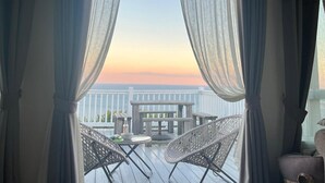 Ein Balkon mit Korbstühlen, einem Tisch und Blick auf den Ozean bei Sonnenuntergang.