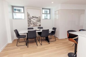 A modern dining area with a white table and black chairs, two windows, and a large abstract painting on the wall. - Azzure Bliss at Bokarina Beach (Bokarina)