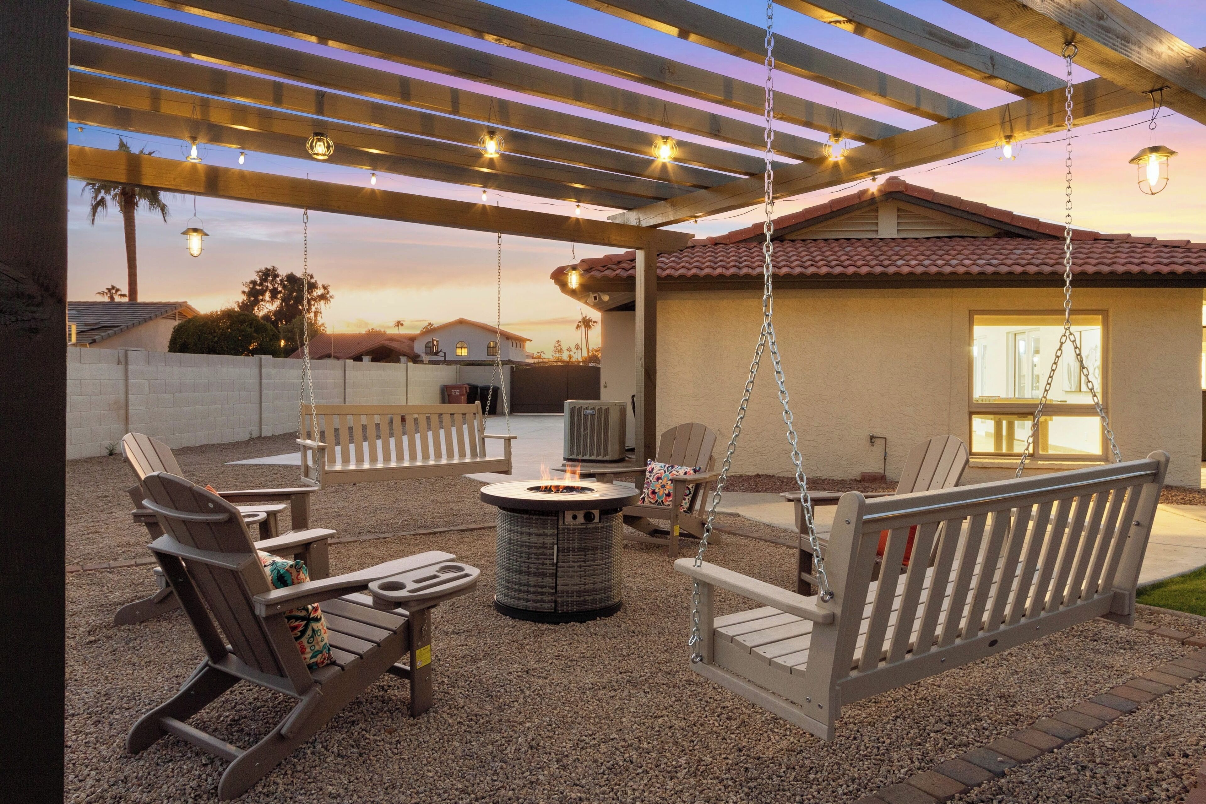 Uma área de pátio externa com lareira, assentos e uma pérgola decorada com luzes de corda.