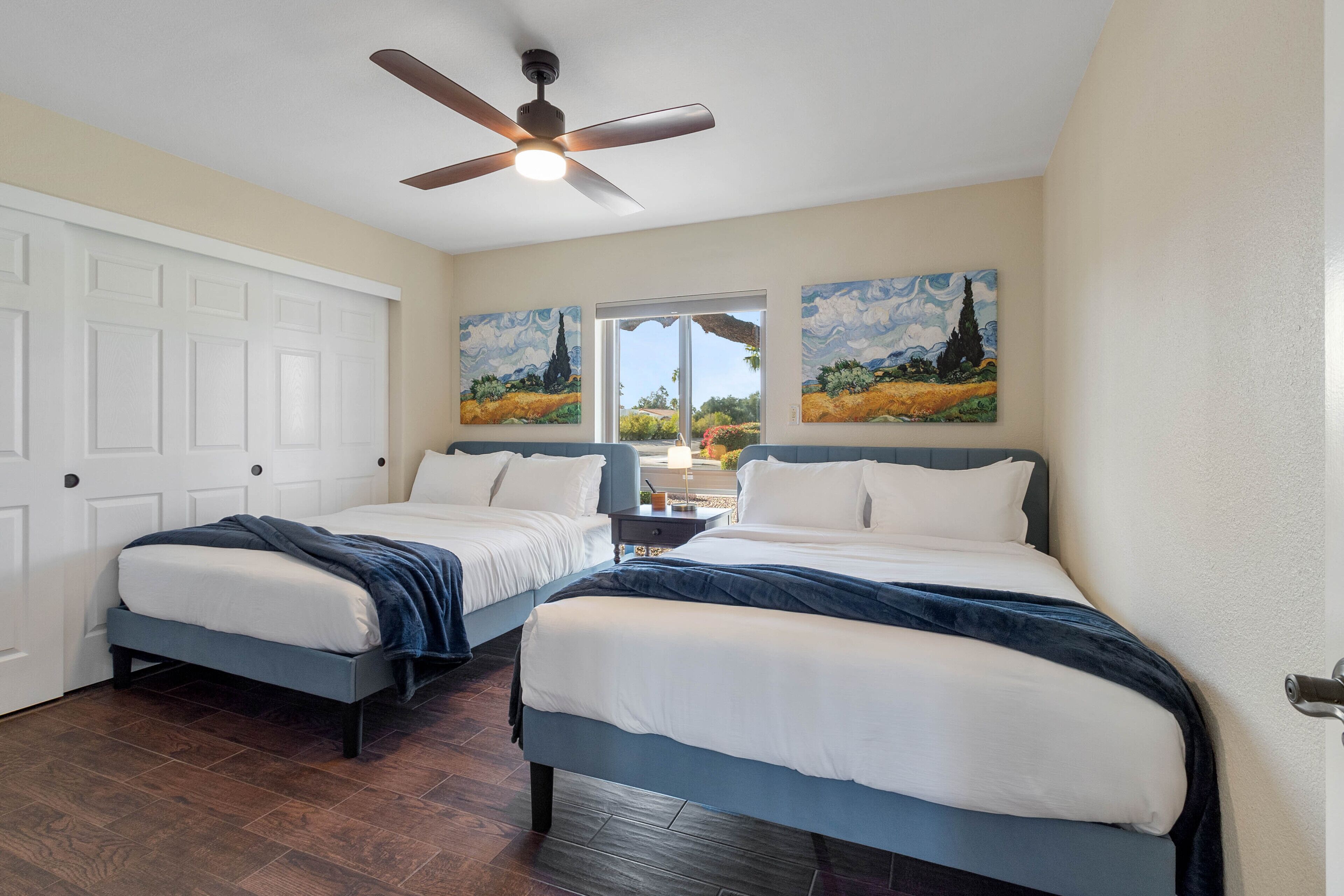 A bedroom with two beds, a ceiling fan, and two paintings on the wall.