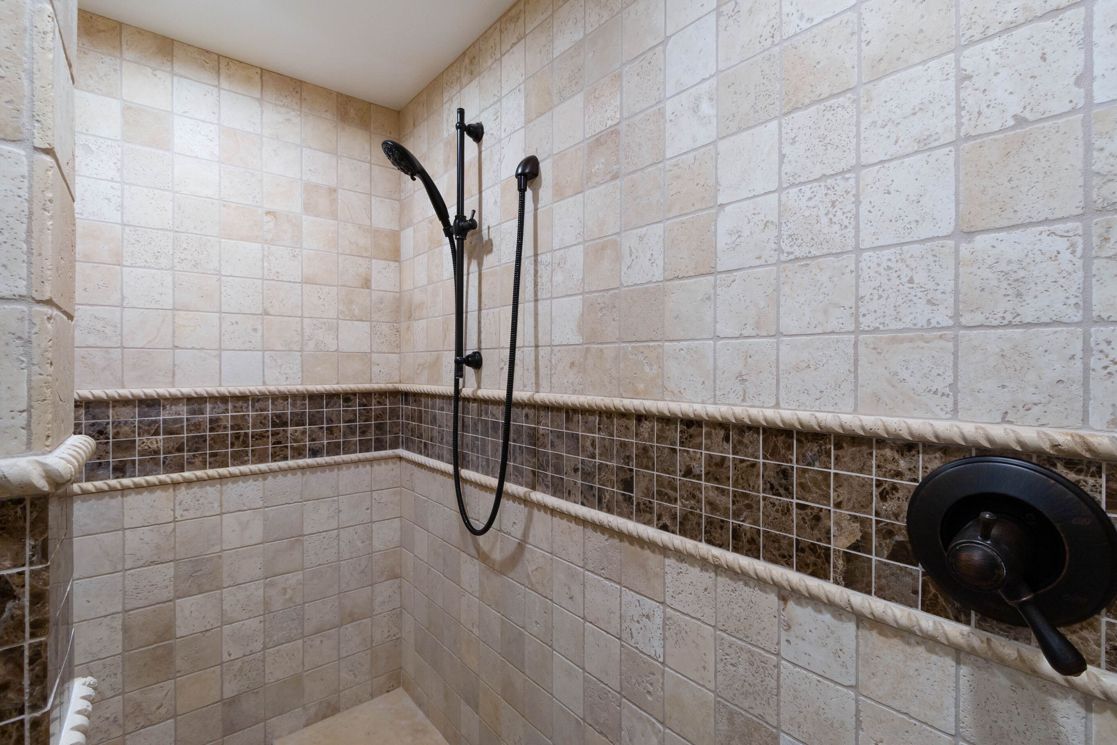 A shower area with beige tiles, a black showerhead, and a control knob.