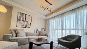 A modern living room with a sofa, armchair, coffee table, and artwork on the wall. - Mynt Stay zed west Residence (Sheikh Zayed City)