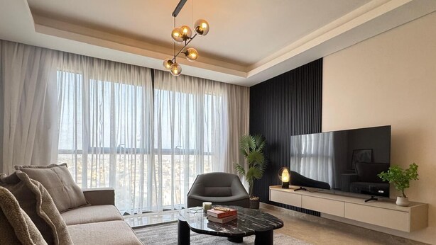 A modern living room with a sofa, a coffee table, a TV, and a plant. - Mynt Stay zed west Residence (Sheikh Zayed City)