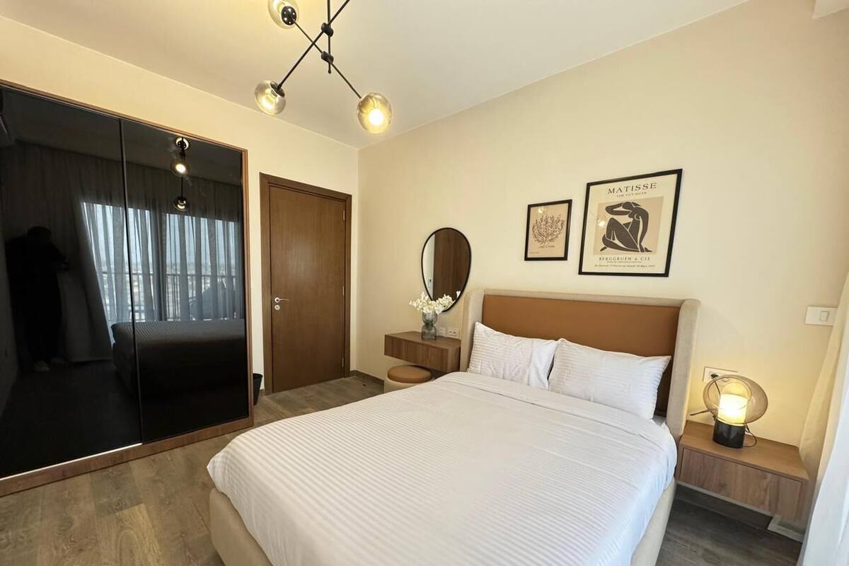 A hotel room with a large bed, a mirror, a bedside table with a lamp, and artwork on the wall.