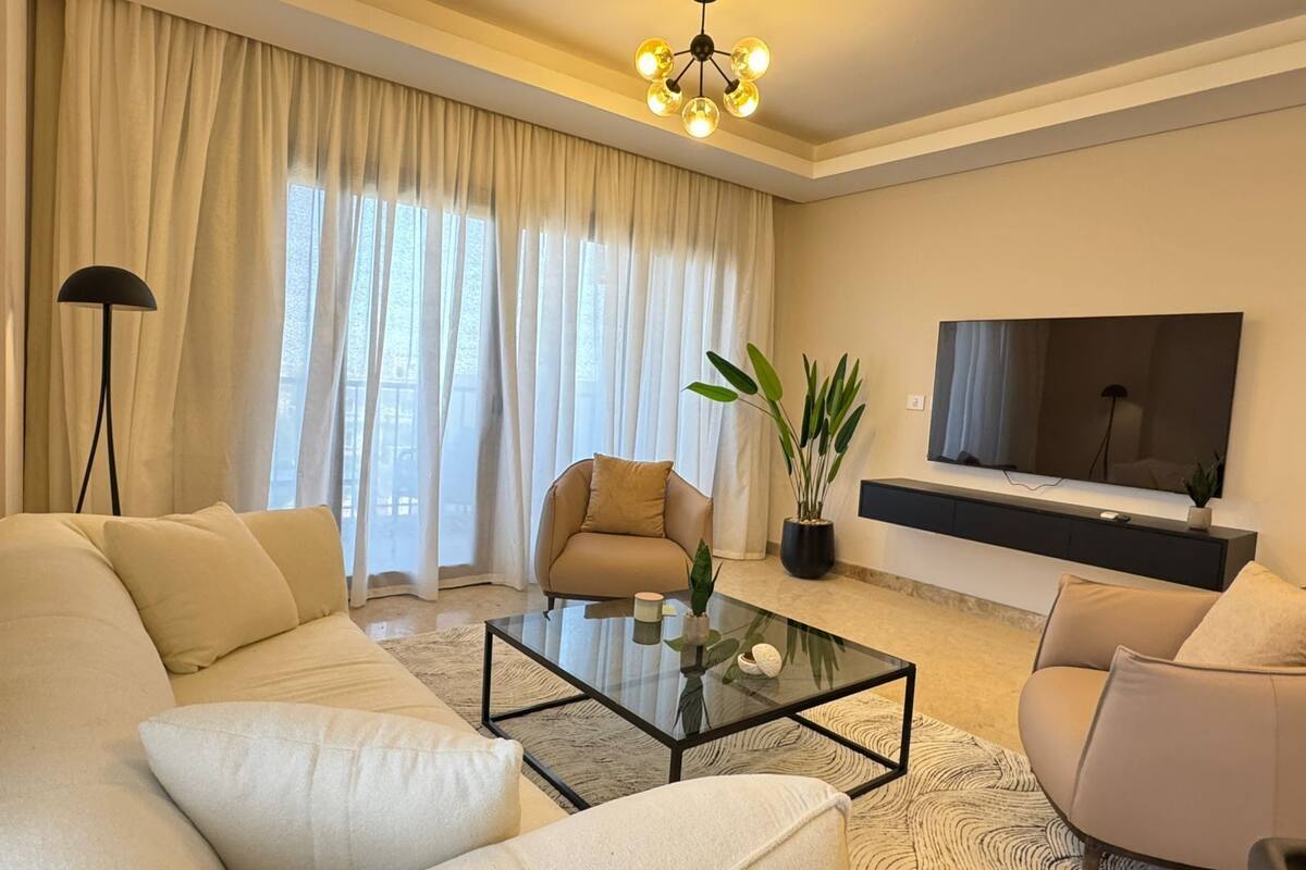 A modern living room with a sofa, armchair, coffee table, and a TV mounted on the wall.