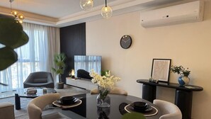 A modern dining area with a glass table, black and white chairs, a vase with flowers, and a black clock on the wall. - Mynt Stay zed west Residence (Sheikh Zayed City)
