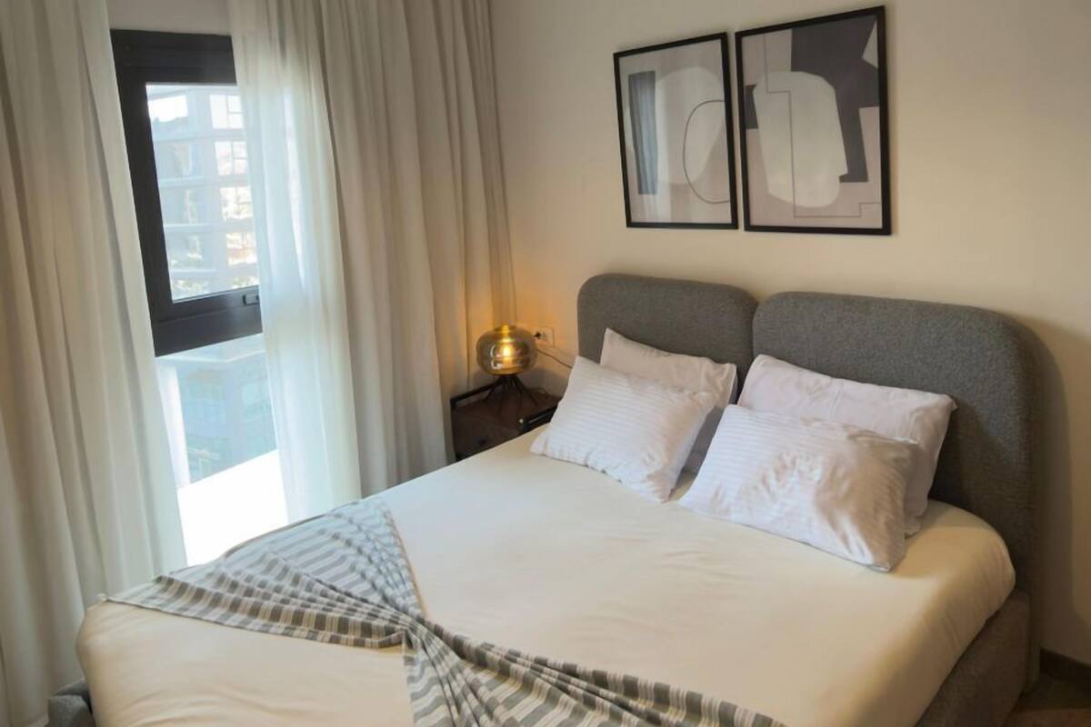 A modern hotel room with a large bed, a bedside lamp, and a window with curtains.