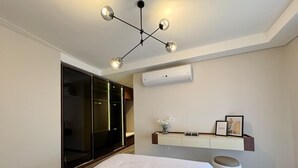 A modern bedroom with a large bed, a wardrobe, a vanity with a mirror, and a ceiling light fixture. - Mynt Stay zed west Residence (Sheikh Zayed City)