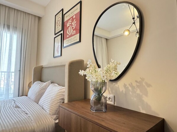 A hotel room with a bed, a bedside table with a vase of flowers, a round mirror, and artwork on the wall. - Mynt Stay zed west Residence (Sheikh Zayed City)