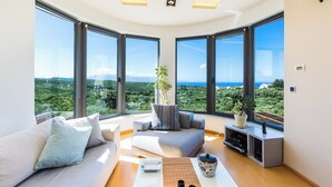A modern living room with a large window, a sofa, a coffee table, and a small plant.