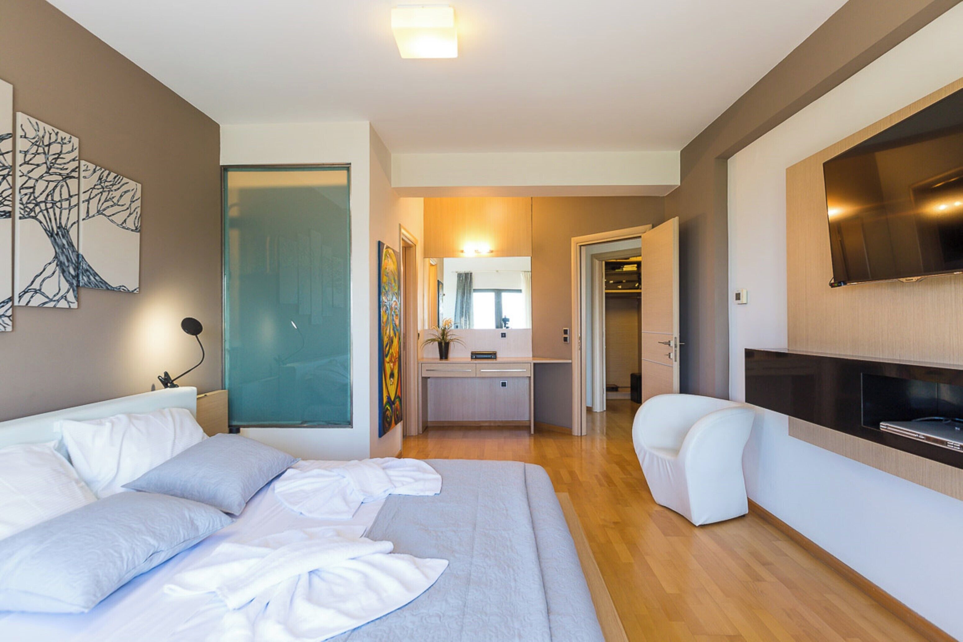 A modern hotel room with a large bed, a sofa, a TV, and a desk with a mirror.
