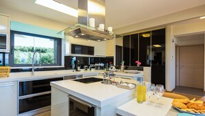 A modern kitchen with a central island, built-in appliances, and a large window offering a view of greenery.