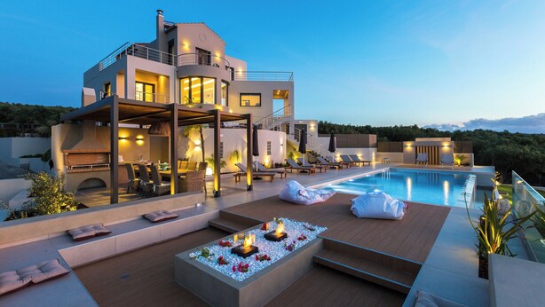 A modern villa with a swimming pool, outdoor seating, and a well-lit patio area.