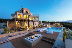 Una vila moderna amb piscina, seients exteriors i una zona de terrassa ben il·luminada.