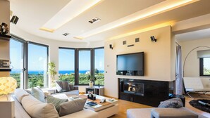 A modern living room with a fireplace, large windows, and a flat-screen TV.