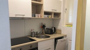 A compact kitchen with a dishwasher, oven, and a small countertop with a toaster and utensils. - Cozy studio in beautiful Budapest with WiFi, AC (Budapest)