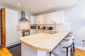 Una cocina moderna con armarios blancos, encimera de madera, campana extractora de acero inoxidable y horno integrado.