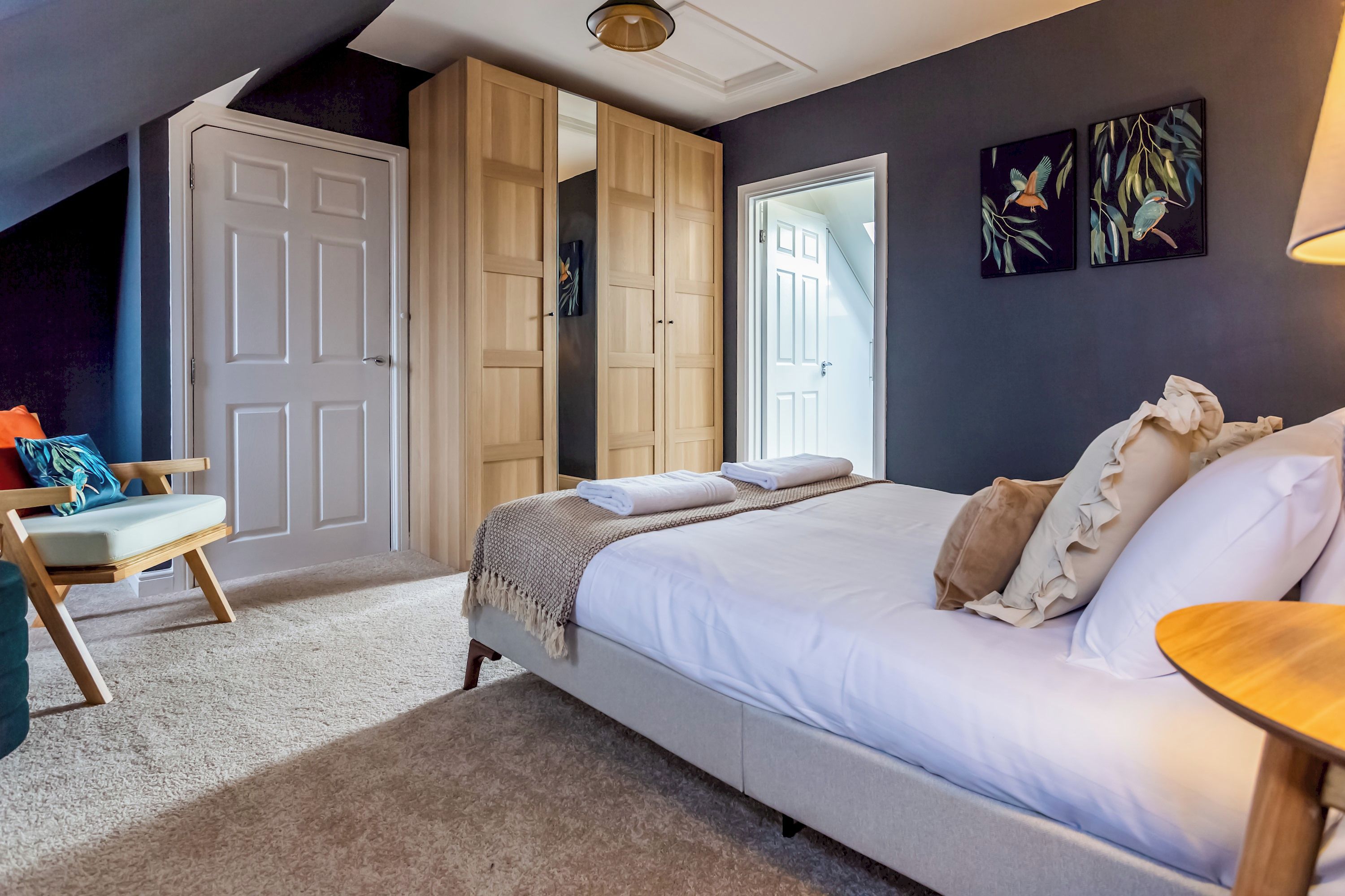 A bedroom with a bed, a chair, a wardrobe, and artwork on the wall.