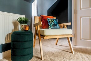 Una habitación con una silla de madera, un reposapiés verde y una planta en maceta.