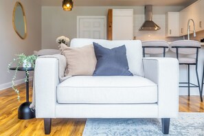 Una sala de estar moderna con un sofá, una mesita auxiliar con una planta y una cocina al fondo.