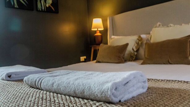 A neatly made bed with a folded towel, a bedside lamp, and two wall-mounted paintings. - Hallgarth Street  (Sherburn Village)