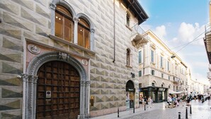A historic building with a large wooden door and arched windows, a cobblestone street, and pedestrians. - Palazzo Confalonieri da Lisca (Verona)
