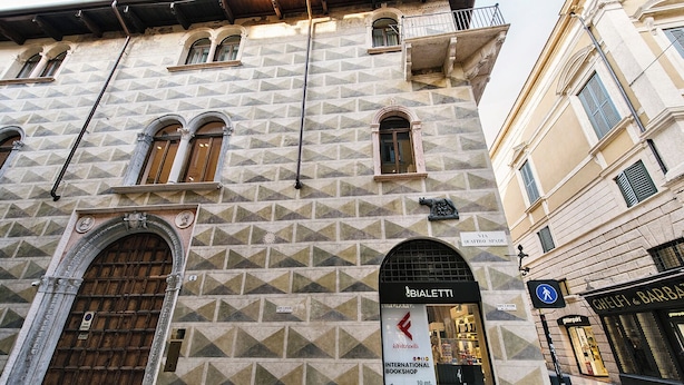 A building with a geometric facade, a large wooden door, and a sign for BIALETTI INTERNATIONAL BOOKSHOP. - Palazzo Confalonieri da Lisca (Verona)